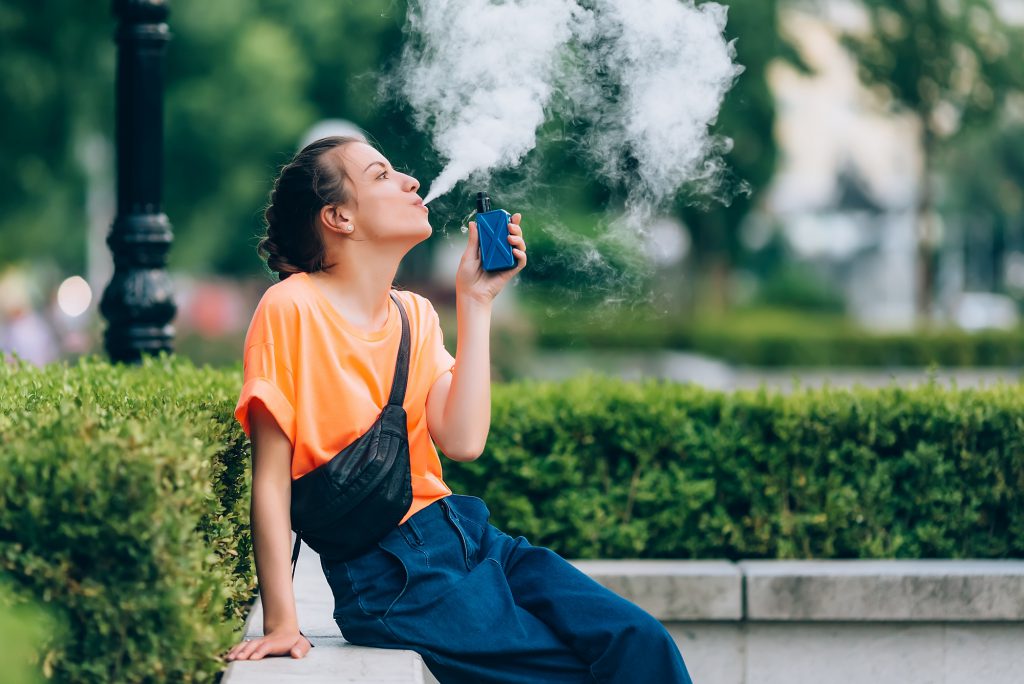 Pretty young girl vape popular ecig gadget,vaping device.Happy brunette vaper girl with e-cig.Portrait of smoker female model with electronic cigarette vaporizer.Ejuice vaping with fruit flavor liquid