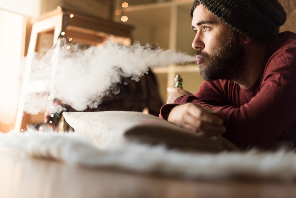 Young man with a knit cap using a vaper